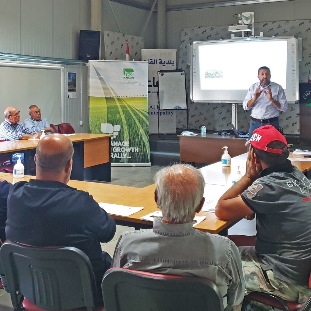 A Natagri trainer speaking with farmers seated around a meeting table